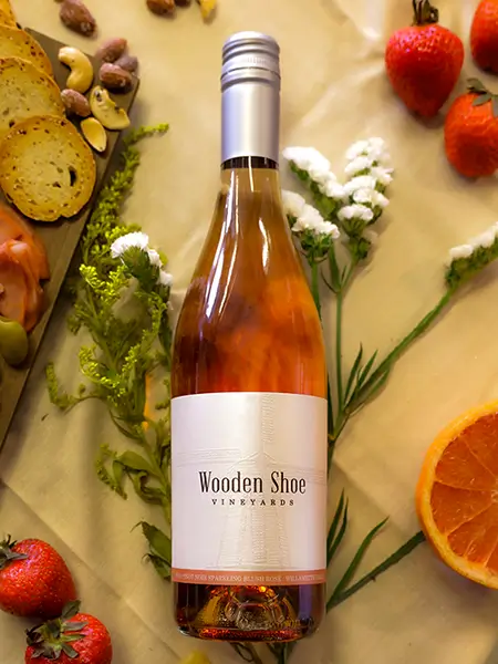 A bottle of Wooden Shoe Vineyards wine atop an elegant table with fruits, flowers, & nuts